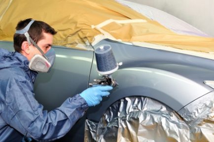 Worker painting a silver car in a paint booth.